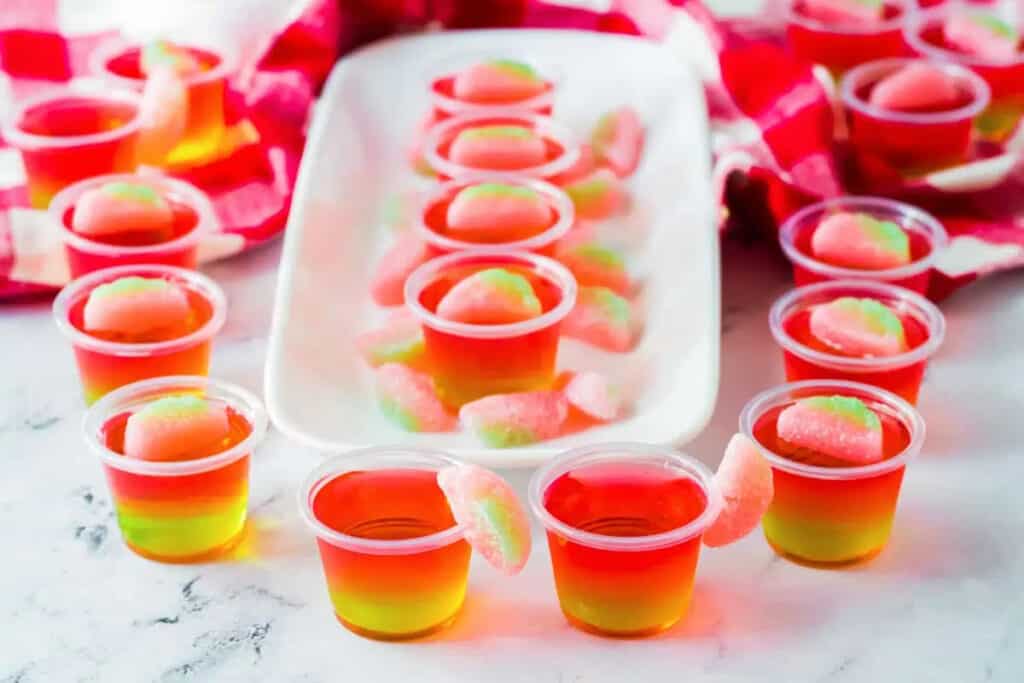 Green and pink jello shots with candy on top.