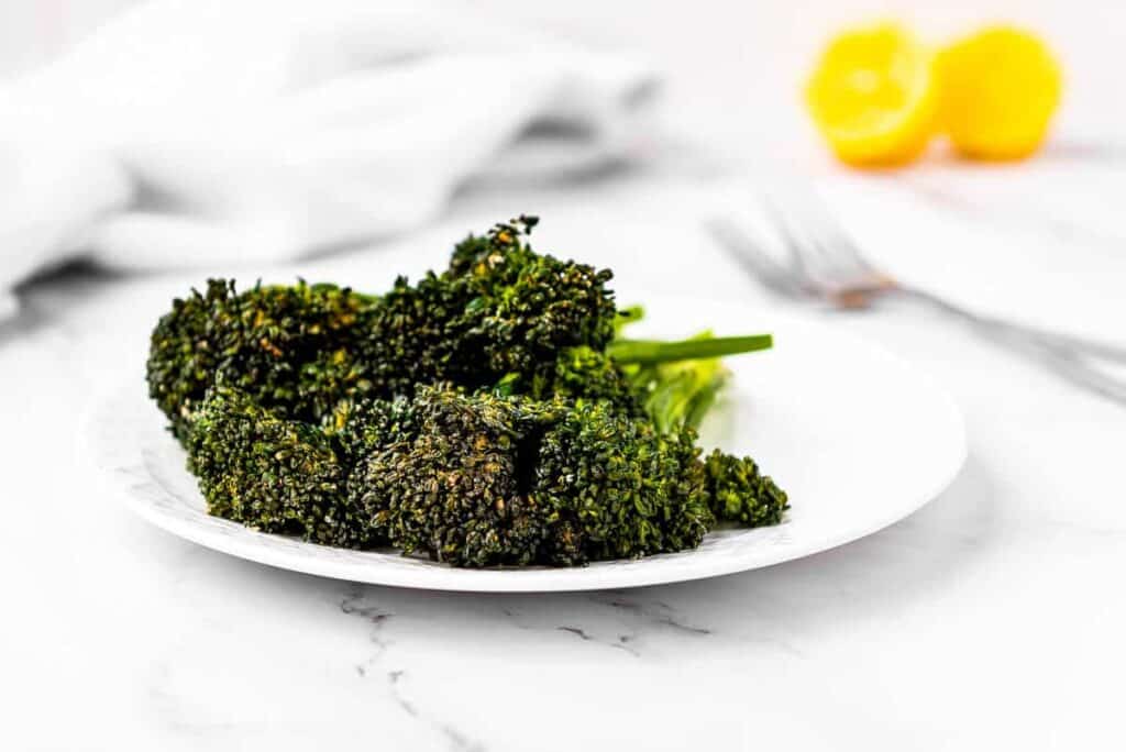 Air fried broccolini on a plate with lemons in the background.