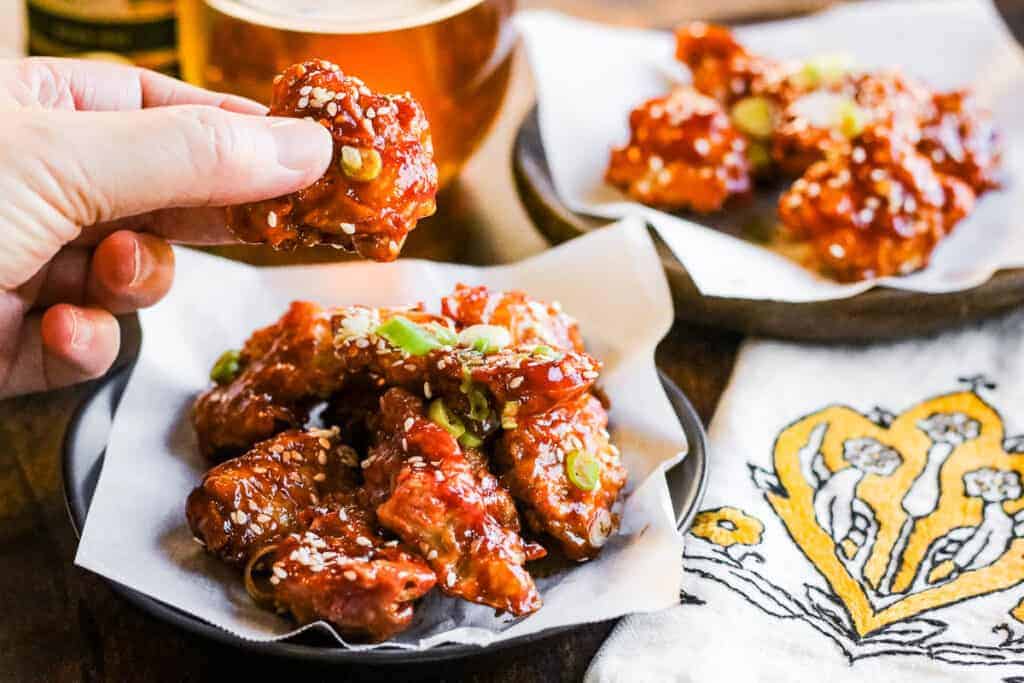 A plate of Air Fryer Korean Fried Chicken with a hand holding up a piece of chicken.