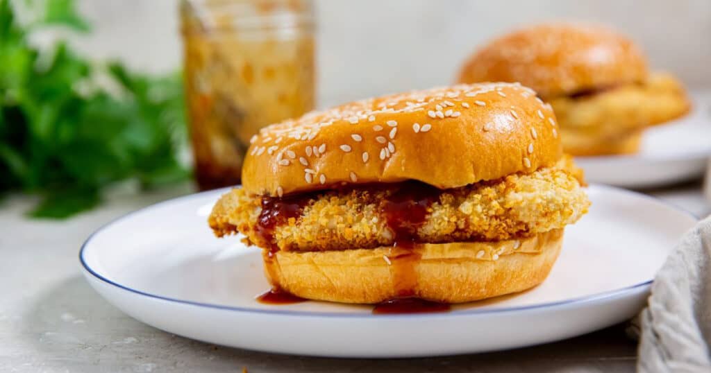 Air fryer chicken katsu sandwich on a white plate with katsu sauce and parsely in the background