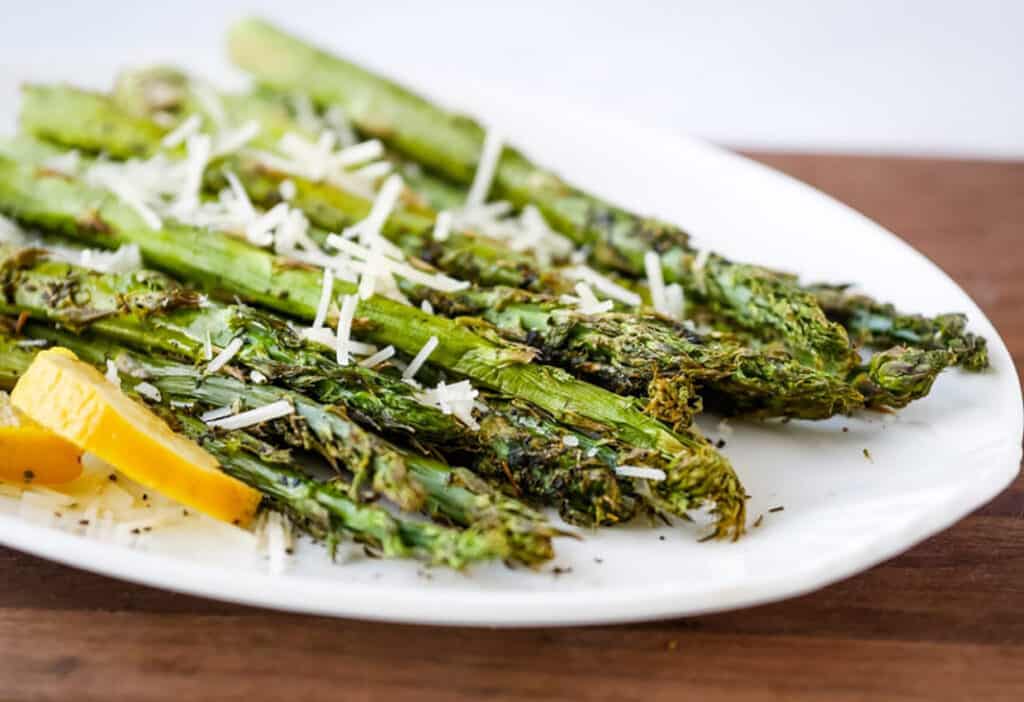 Air Fryer Asparagus on a white platter with lemon slices and Parmesan.