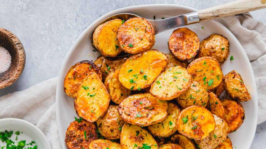 Golden roasted air fryer baby potatoes on a serving plate with a wooden and metal spoon.