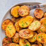Golden roasted air fryer baby potatoes on a serving plate with a wooden and metal spoon.