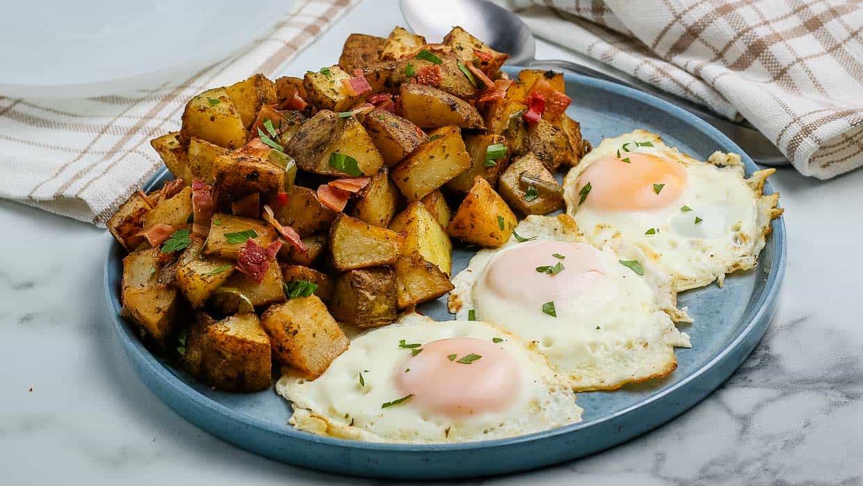 Breakfast potatoes on a plate with 3 eggs.
