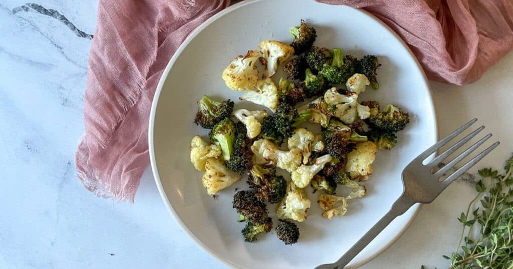 air fryer broccoli and cauliflower on a white plate with a pink linen and thyme.