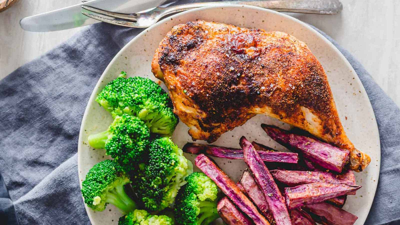 Air fryer chicken leg quarters on a plate with broccoli and purple sweet potato fries.