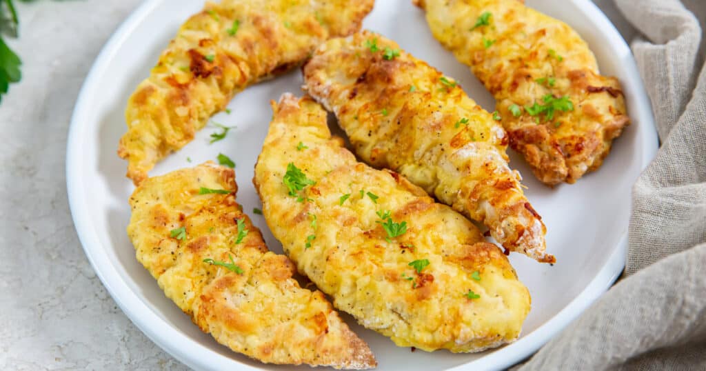 5 air fryer chicken tenders with flour on a white plate with a brown napkin topped with parsley