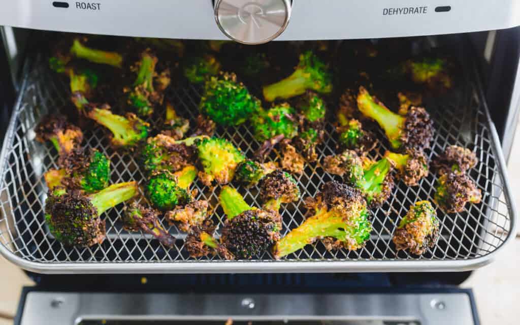 Frozen broccoli florets roasted on an air fryer tray.