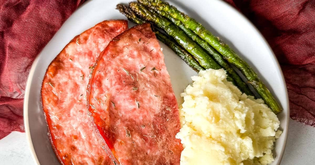 Air fryer ham steak with asparagus and mashed potatoes on a white plate.