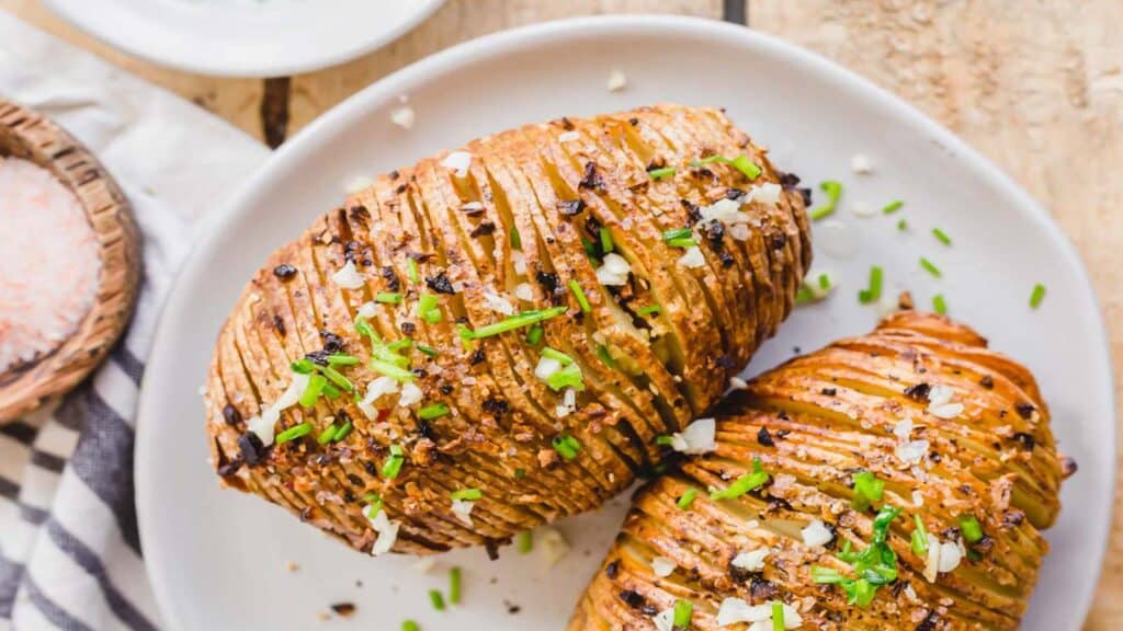 Two crispy air fryer hasselback potatoes with chives, garlic and butter on a white plate.