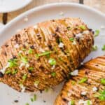 Two crispy air fryer hasselback potatoes with chives, garlic and butter on a white plate.