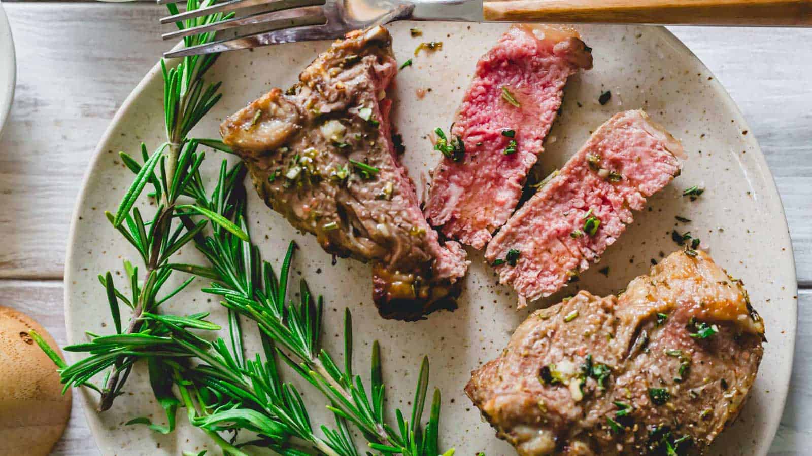 Air fryer lamb chops sliced on a plate with fresh rosemary sprigs.
