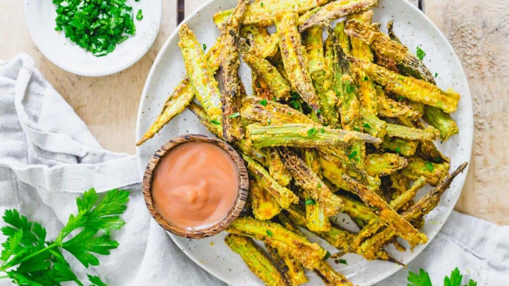 Spiced air fryer okra fries served with a yogurt dip on a plate with fresh parsley.
