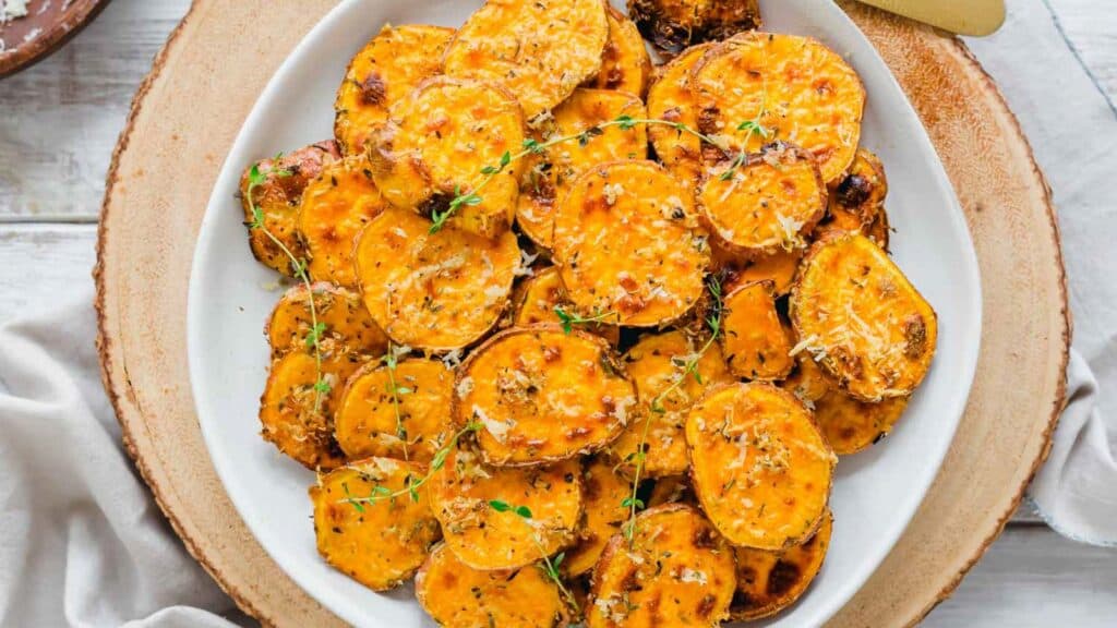 Air fryer sweet potato rounds with a parmesan herb crust garnished with thyme sprigs on a plate.