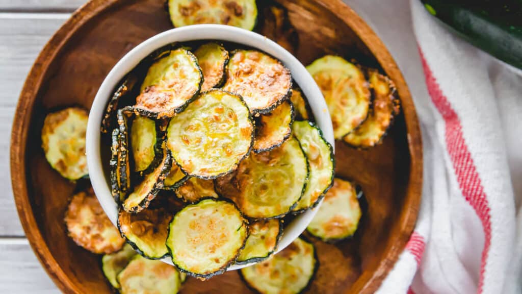 Zucchini chips without breading made in the air fryer in a bowl on a wooden plate.