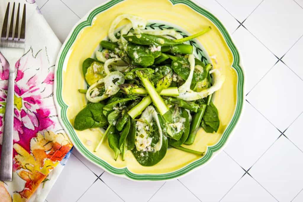 Asparagus and salad greens in a green and yellow bowl.