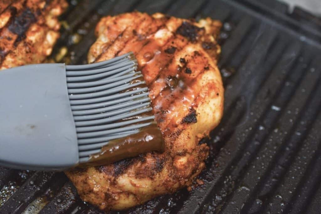 Basting BBQ sauce on grilled boneless chicken thighs.