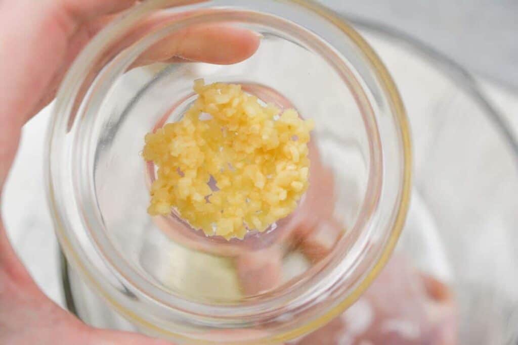 Adding minced garlic to chicken in bowl.