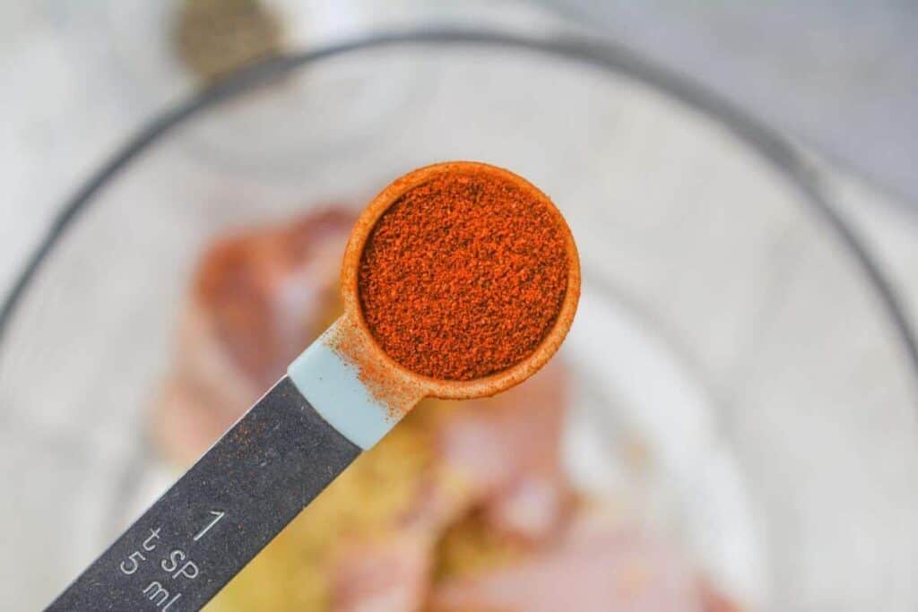 Adding paprika to chicken in bowl.