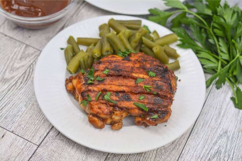 Grilled chicken thigh on white plate with green beans.