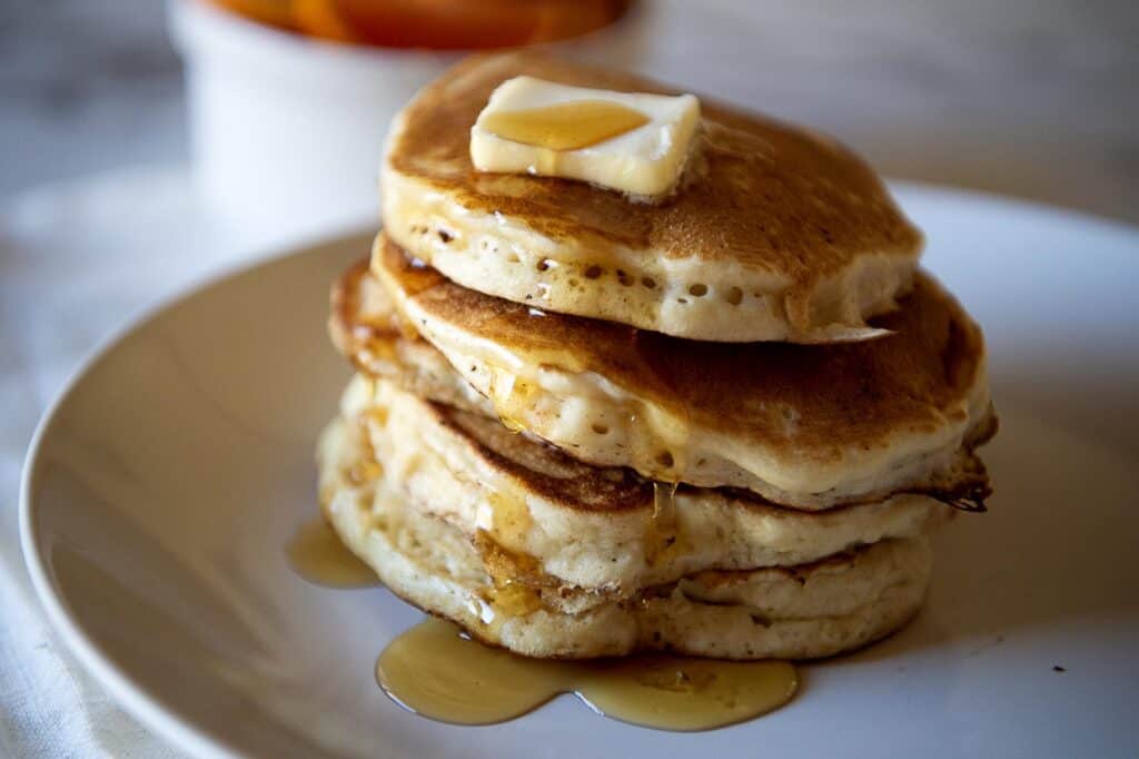 A stack of pancakes with butter and syrup on a plate.