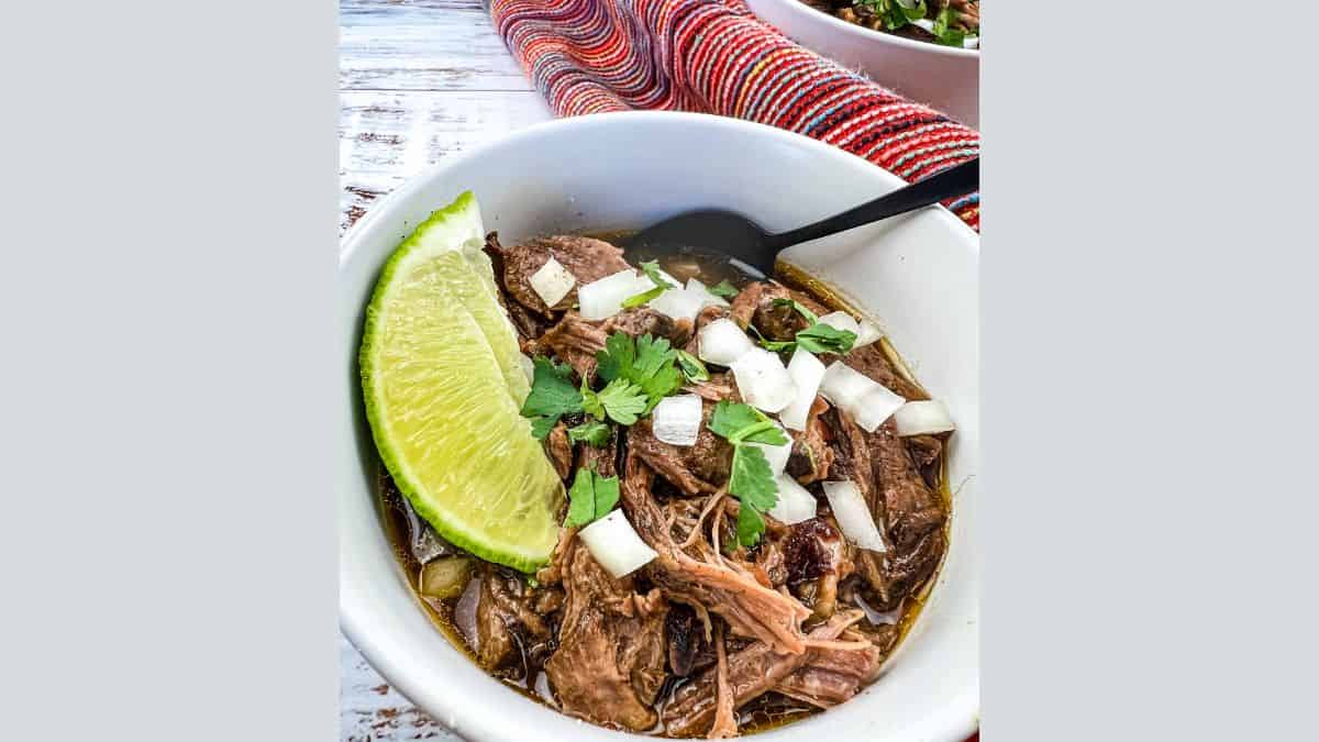 Two white bowls filled with slow cooker birria garnished with fresh lime wedges.