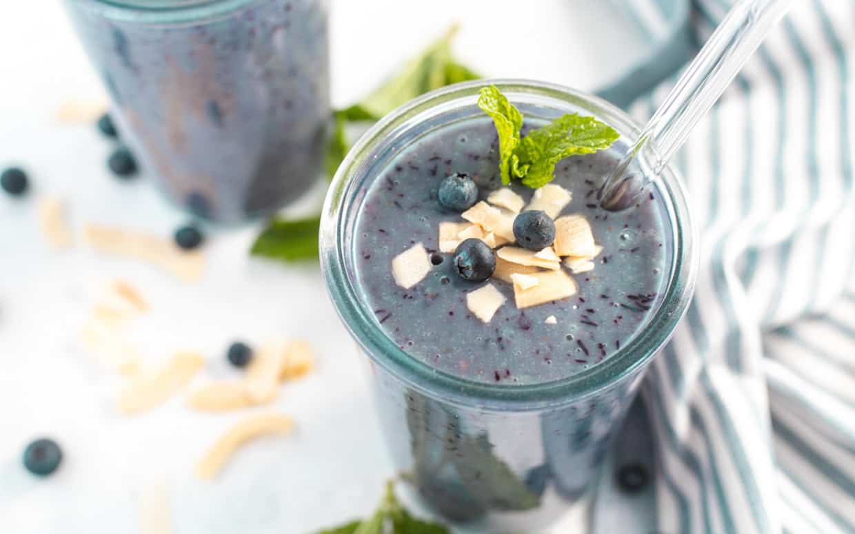 Glass of blueberry mango smoothie with coconut flakes and mint.