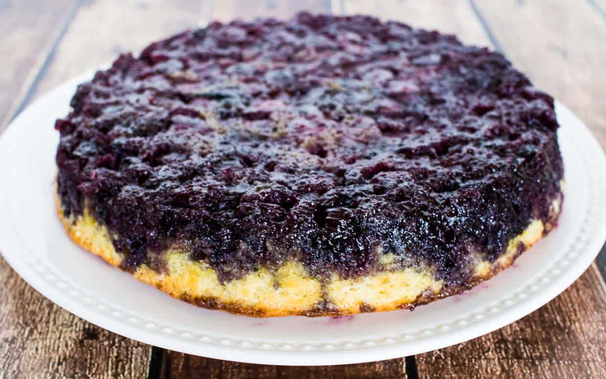 Blueberry upside down cake on a white plate before slicing.