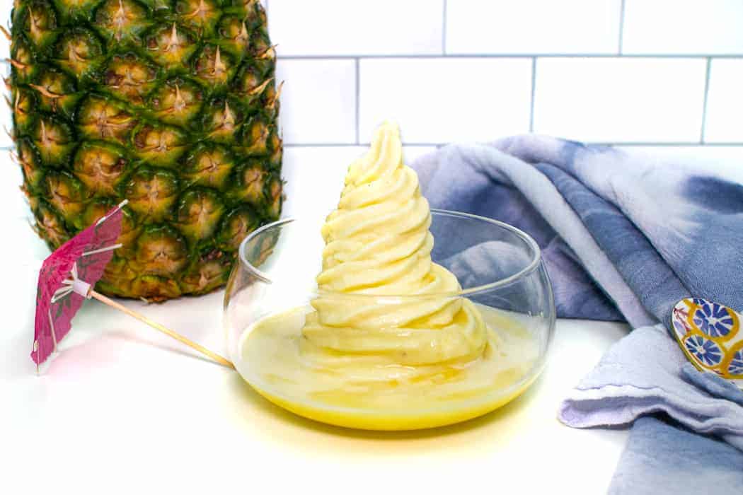 dole whip in a glass bowl next to a pineapple.