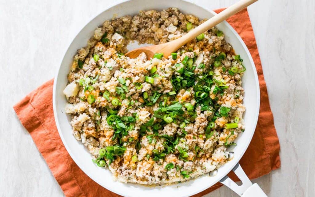 White skillet with buffalo ground turkey and cauliflower rice with a wooden spoon.