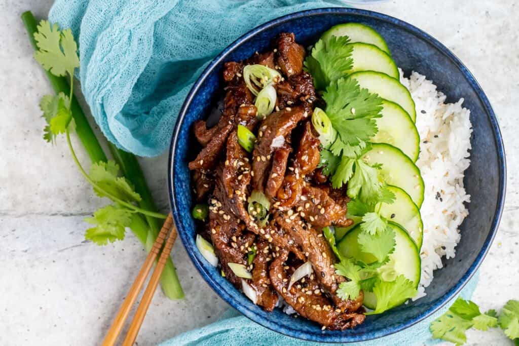 Bulgogi in a bowl with cucumber slices, rice, and cilantro.