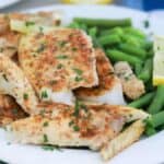 Baked butter fish on a plate with green beans.