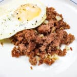 Canned corned beef hash on a plate with a fried egg.