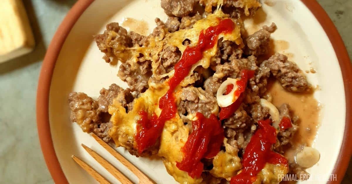 A picture of ketchup over cheesy onion and ground beef skillet dinner.