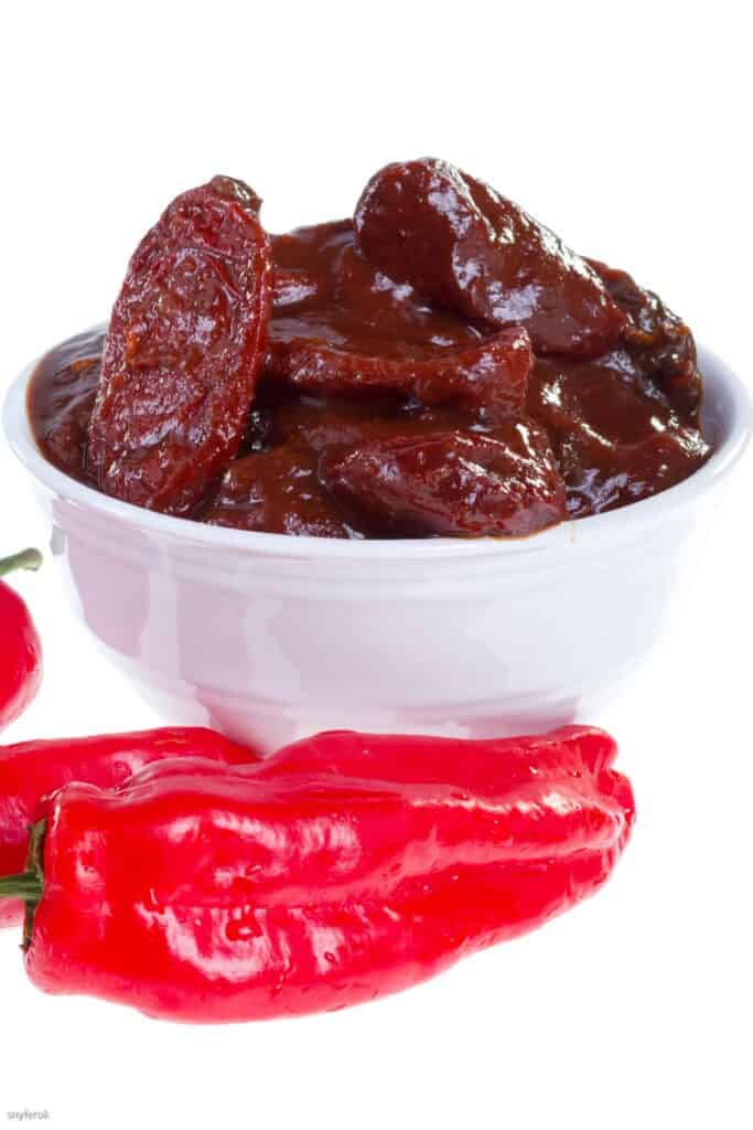 Chipotle peppers in a bowl with fresh red peppers on the side.