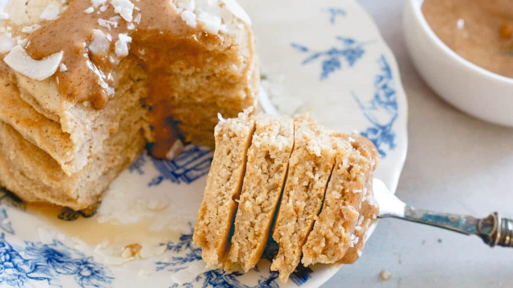 Doughy coconut flour pancakes with almond butter sauce topping and flaked coconut.