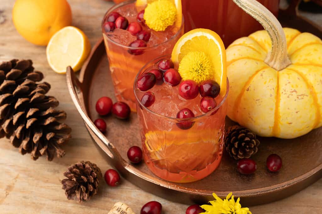 Glasses filled with an orange beverage garnished with cranberries and flowers.