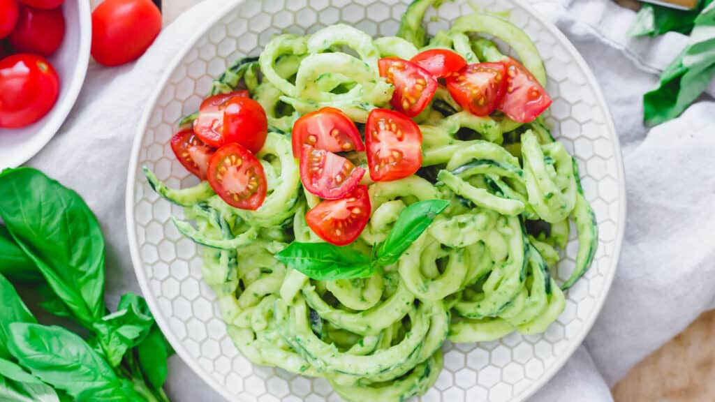 Zucchini noodles with creamy avocado sauce and cherry tomatoes in a bowl.