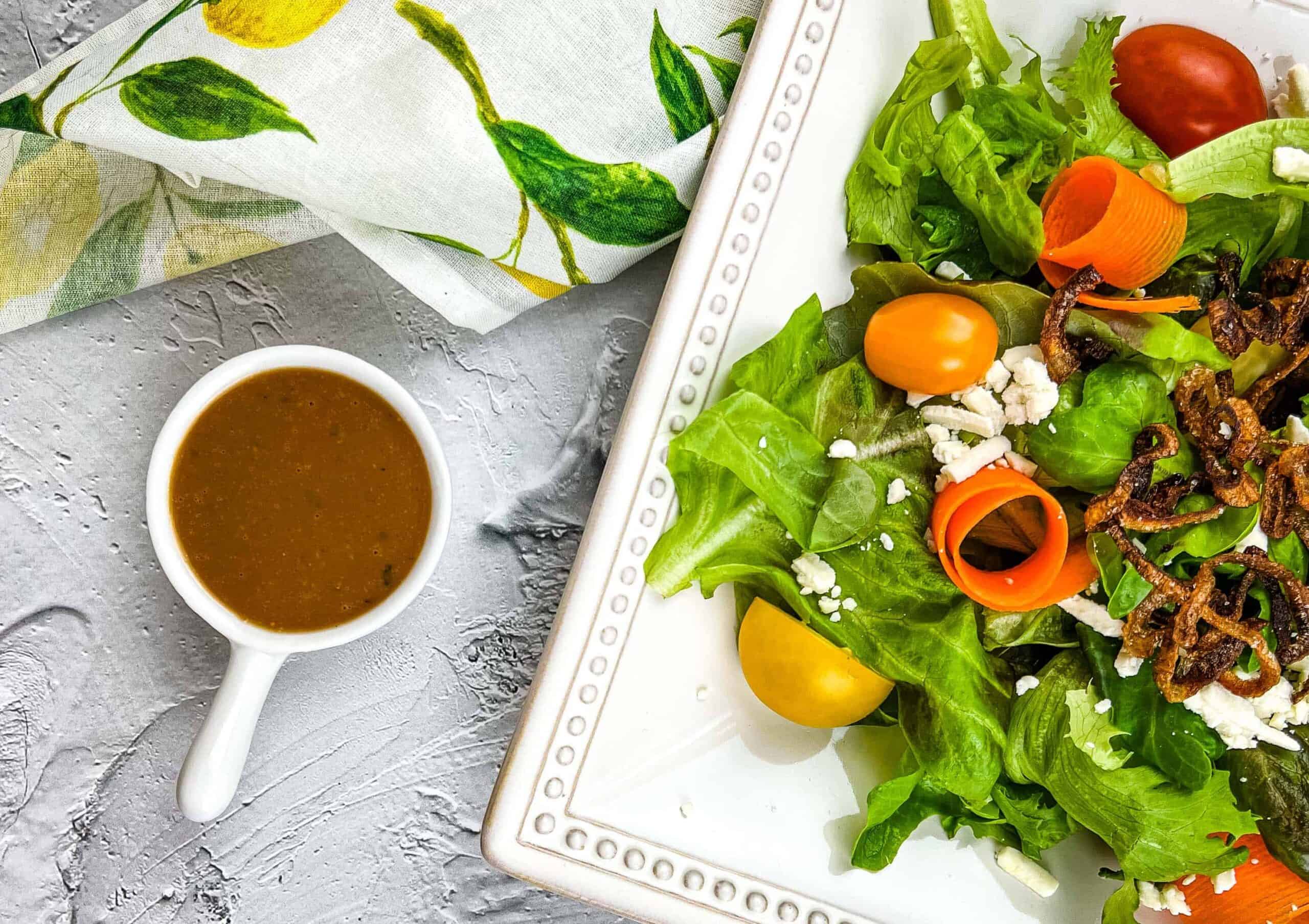 A white plate of creamy balsamic vinaigrette salad dressing resting next to a plate of salad.