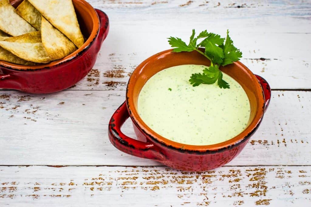 Creamy Jalapeno Dip in a bowl with chip nearby.