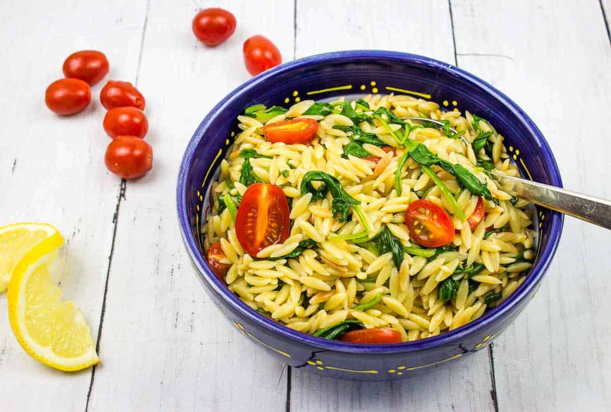 Creamy spinach orzo in a blue bowl with tomatoes nearby.
