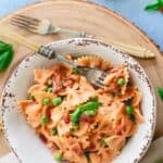 Creamy tomato farfalle with peas and prosciutto in a white bowl.