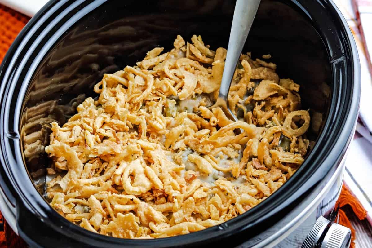 Slow cooker with green bean casserole topped with fried onions.