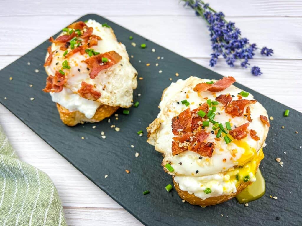 Two slices of Cottage Cheese Toast with Eggs & Bacon on a black platter.