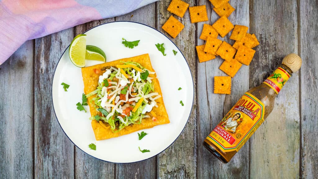 Cheez-It Tostada on a plate with hot sauce in a bottle.