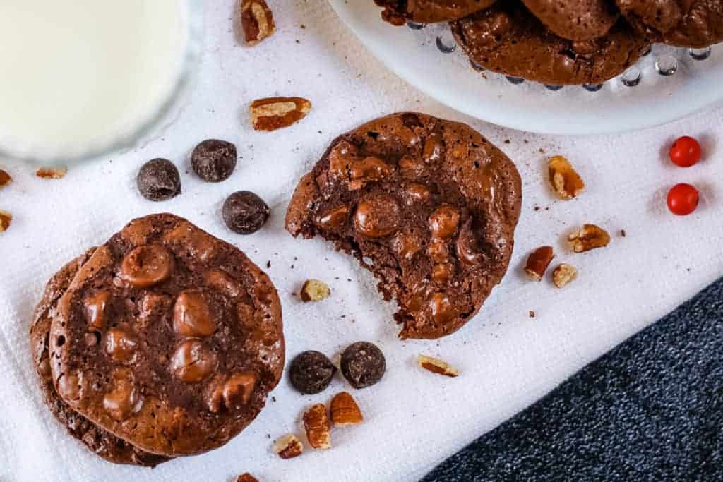 Flourless chocolate cookies on a white linen with chocolate chips and pecans.