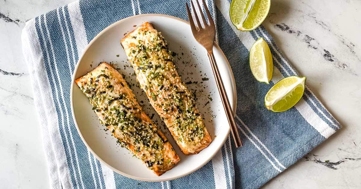 two fillets of furikake salmon on a white plate surrounded by lime slices.