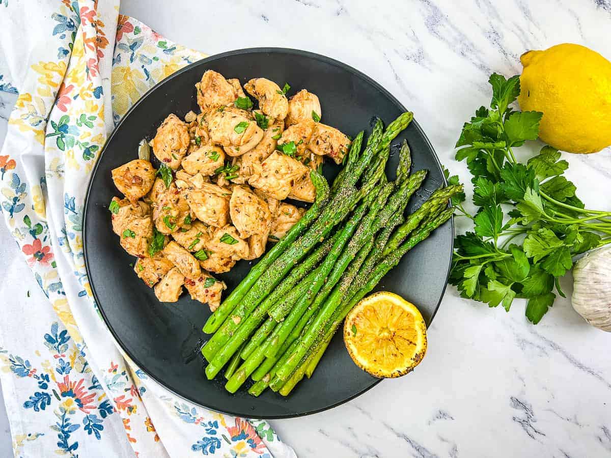 Black plate of chicken with asparagus.