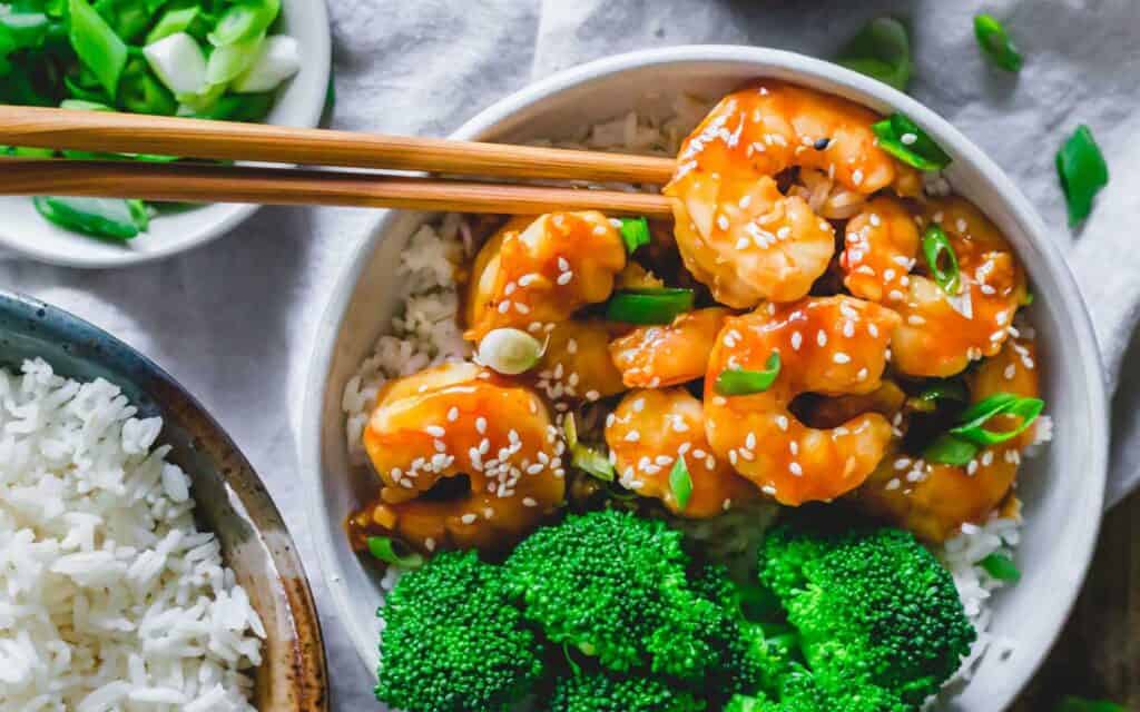 Homemade general tso shrimp with broccoli and rice in a bowl with chopsticks.