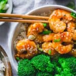 Homemade general tso shrimp with broccoli and rice in a bowl with chopsticks.